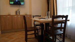 Un comedor con una mesa y sillas de madera, un televisor en la pared y un mueble con cajones.