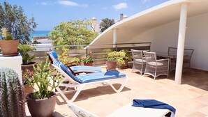 Une terrasse agrémentée de chaises longues et d’une table, entourée de plantes en pot et de cactus.
