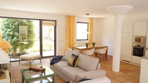 Un salon comprenant un canapé, une table basse et un coin repas avec des chaises et une table. Une porte-fenêtre coulissante donne accès à un jardin.