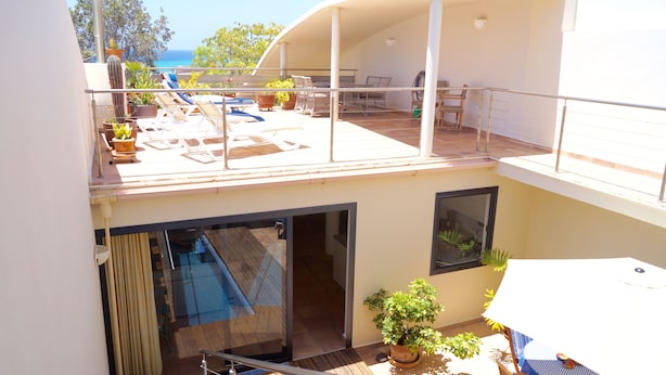 Un bâtiment à deux étages doté d’un balcon, d’un espace extérieur aménagé pour s’asseoir et de plantes en pot.