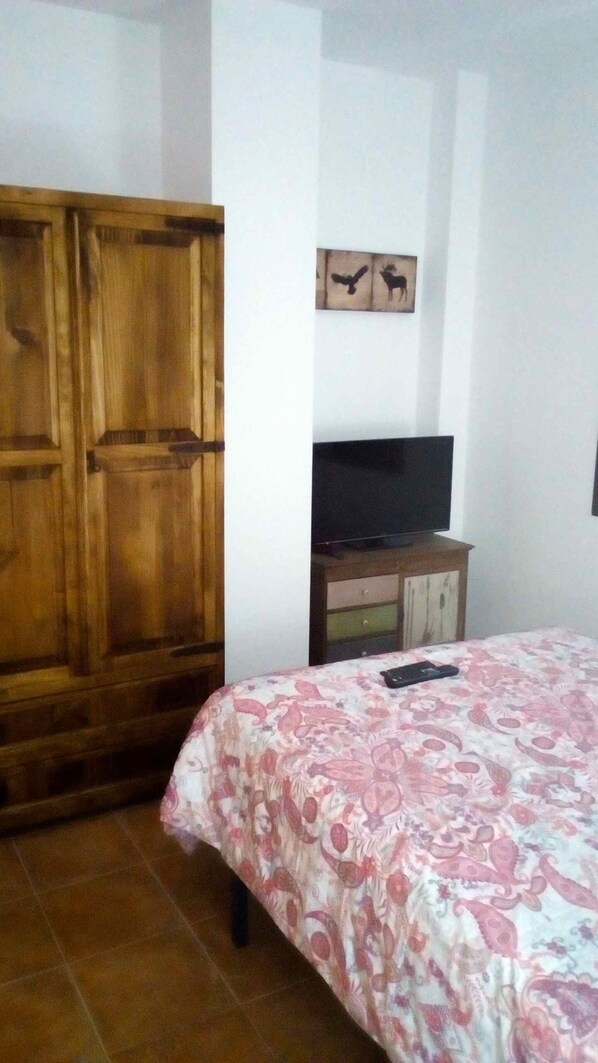 Un dormitorio con un armario de madera, un televisor sobre un mueble de madera y una cama con colcha estampada.
