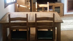 Un coin repas avec une table et des chaises en bois, un téléviseur et une étagère ornée d’objets décoratifs.