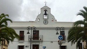 Un bâtiment blanc avec une horloge, une cloche et un panneau indiquant de tourner à gauche.