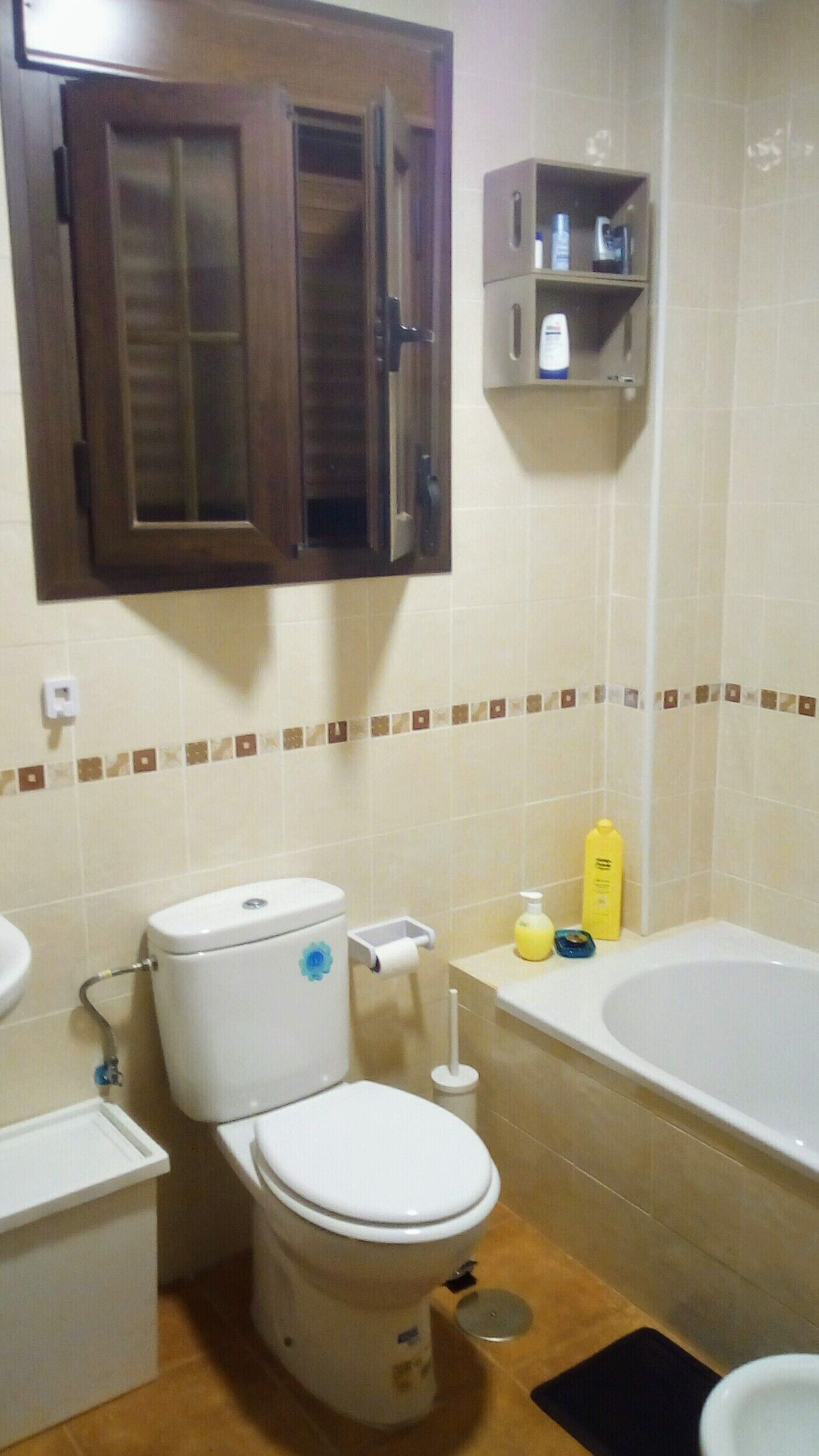 Een badkamer met toilet, wastafel en bad. Daarboven staat een kastje bij het toilet en een plank met toiletartikelen.