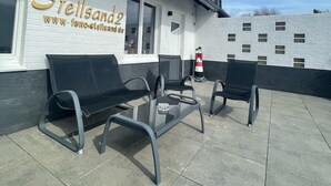 Un área de estar al aire libre con una mesa y sillas frente a un edificio con un letrero que dice "Steilsando".