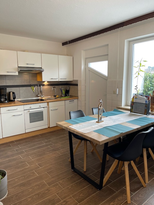 Une cuisine moderne avec des armoires blanches, un four encastré et un coin repas comprenant une table et des chaises.