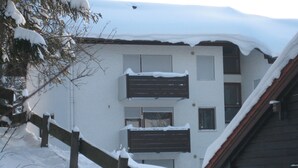 Un edificio de dos pisos con techo nevado y una cerca de madera al frente.