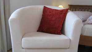 Un sillón blanco con un cojín rojo en una habitación con suelo de madera y una cama con cabecera de madera.