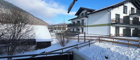 A residential area with snow-covered ground, a wooden fence, and houses with balconies.