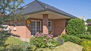 A brick house with a tiled roof, a front porch with chairs, and a well-maintained garden with various plants and flowers. - 4-star holiday home with terrace, large garden, 3 bedrooms and 2 bathrooms (Seebad Heringsdorf)
