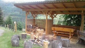 Un pabellón de madera con bancos, una hoguera y una pila de leña.