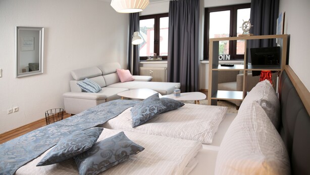 Una habitación de hotel moderna con una cama, un sofá, una mesita y un televisor sobre un soporte de madera.