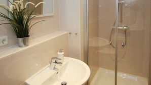 Un baño moderno con cabina de ducha de vidrio, un lavabo blanco y una planta en maceta.