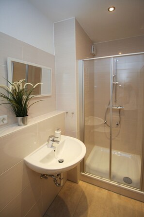 A modern bathroom with a glass shower enclosure, a white sink, and a potted plant. - Schiller-Quartier 15 Apartment no. 3 (Bremerhaven)