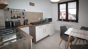 Una cocina compacta con un letrero de café, un hervidor, un tostador y un lavavajillas. Hay un comedor con una mesa y sillas.