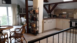 Eine Küche mit Holzschränken, ein Essbereich mit Korbstühlen und ein Bücherregal mit Büchern und Dekoration.