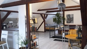 Ein geräumiger Wohnbereich mit hoher Decke, freiliegenden Holzbalken, einem Bücherregal, einem Esstisch und einem Stuhl.