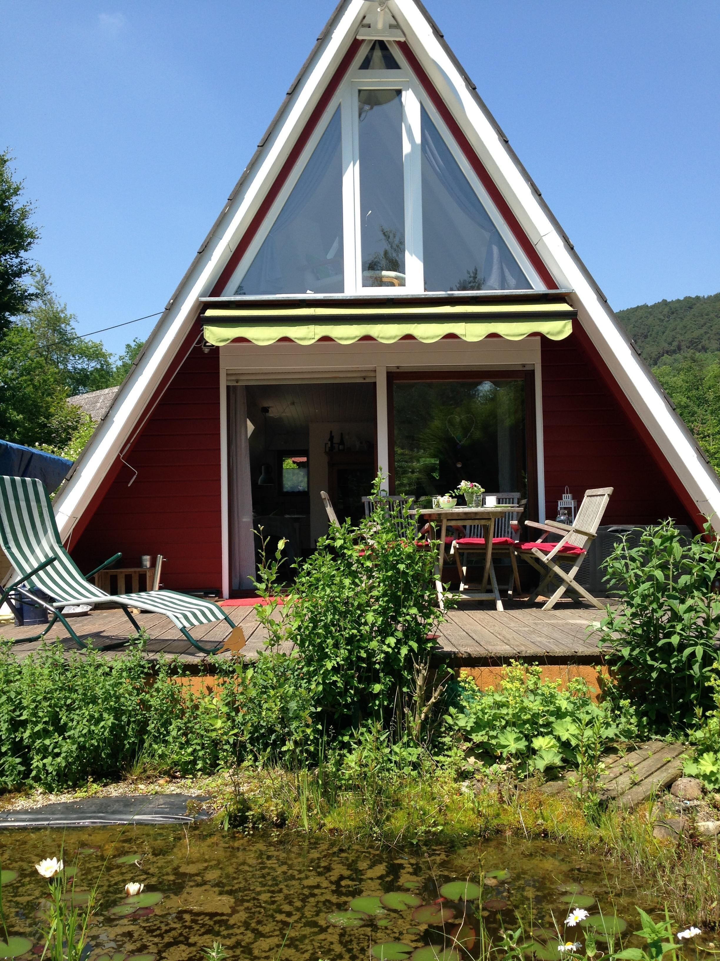 Un bâtiment doté d’un toit triangulaire, d’un patio couvert, d’un espace extérieur aménagé pour s’asseoir et d’un bassin orné de nénuphars.