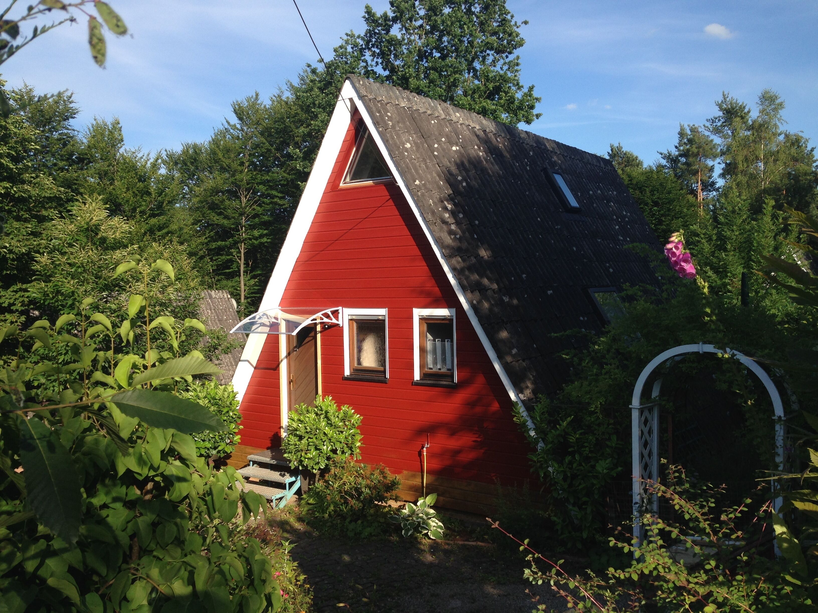 Une maison rouge avec un toit en pente, entourée d’une végétation luxuriante.