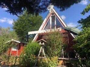 Un bâtiment de forme triangulaire, à la façade rouge et blanche, entouré d’une végétation luxuriante et d’arbres.