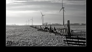 Una hilera de aerogeneradores en un campo nevado, con una valla de madera al frente.