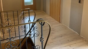 Un escalier orné de rampes en métal conduit à un palier. On aperçoit, au fond, une porte dotée d’une vitre en verre dépoli.