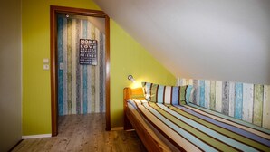 Un dormitorio con techo inclinado, una cama con ropa de cama a rayas, cabecera de madera y una lámpara fijada a la pared.