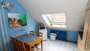 Una pequeña kitchenette equipada con microondas, un refrigerador pequeño y una ventana con persianas.