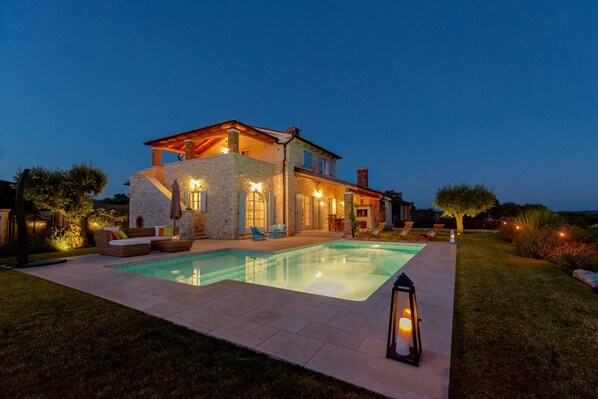Une maison en pierre avec une piscine, un espace salon extérieur et une lanterne.