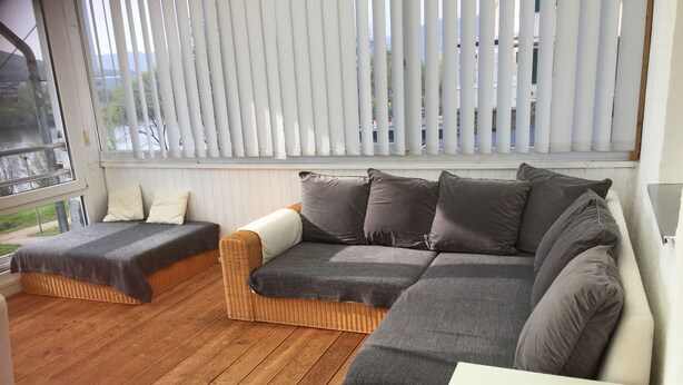 Ein gemütliches Zimmer mit einem Korbssessel, einem kleineren Sofa und einem weißen Tisch mit einem Buch.