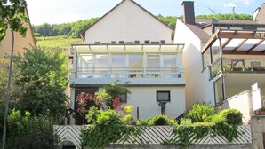 Ein zweistöckiges Haus mit Balkon, umgeben von einer Steinmauer und verschiedenen Pflanzen.