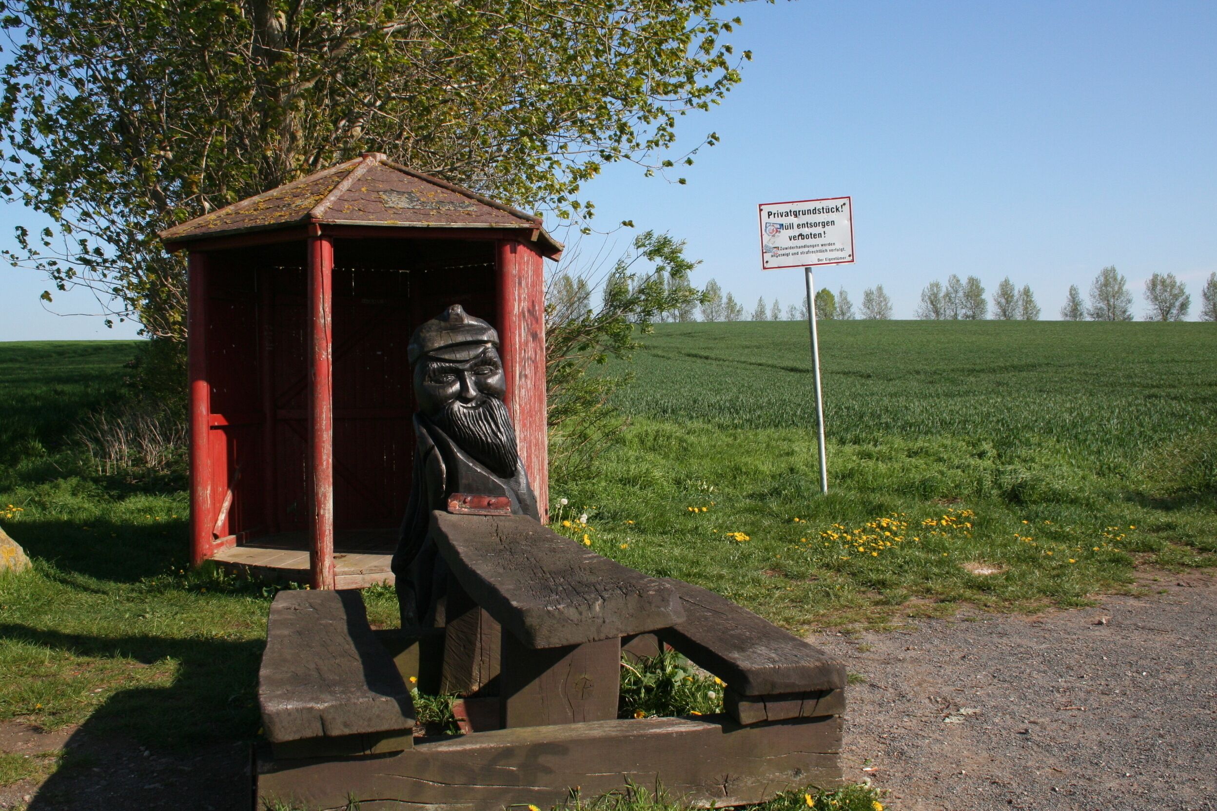 Une structure rustique en bois, comprenant un banc, un panneau et une sculpture représentant un homme.