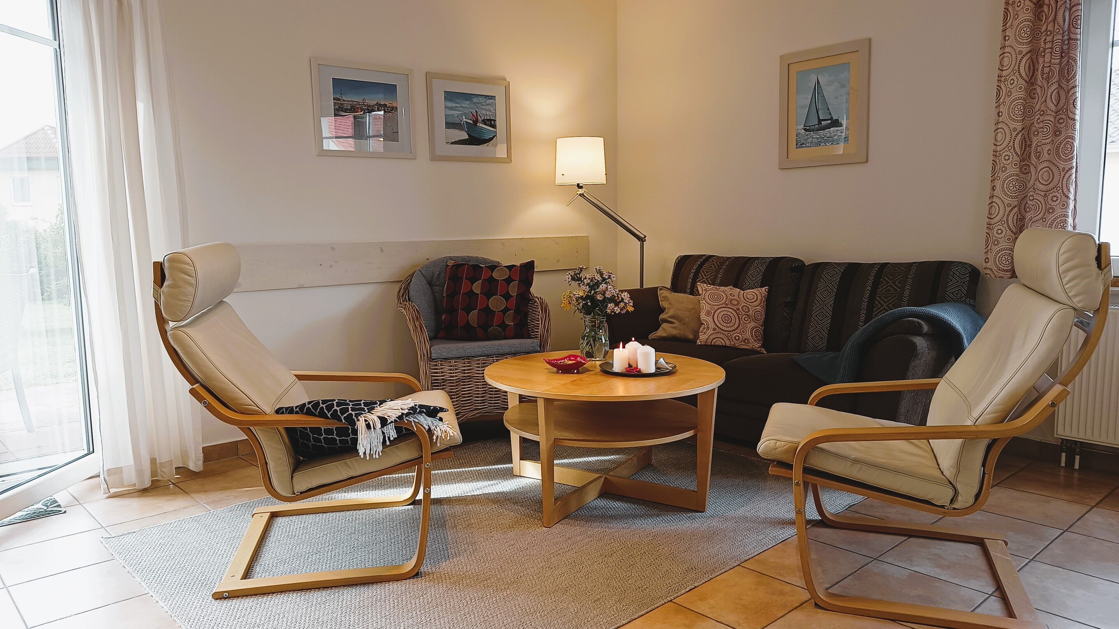 Un salon comprenant un canapé, deux fauteuils, une table basse et un lampadaire. Trois tableaux encadrés ornent le mur.