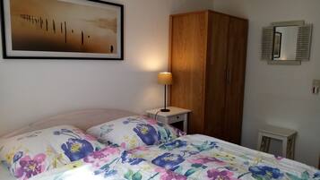 Une chambre à coucher comprenant un lit, une table de chevet, une armoire en bois, un miroir fixé au mur et un tableau encadré.