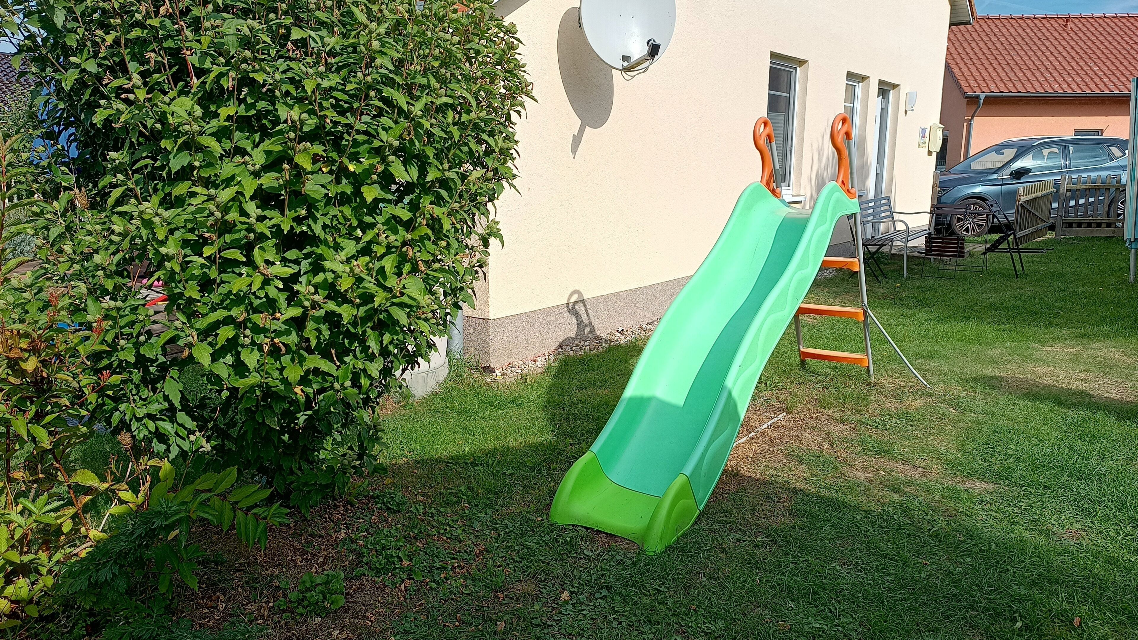 A green slide set up in a grassy yard next to a building with windows and a satellite dish.