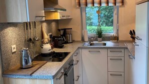 Eine moderne Küche mit weißen Schränken, einer Granit Arbeitsplatte, Edelstahlgeräten und einem Fenster mit Blick auf Grünflächen.