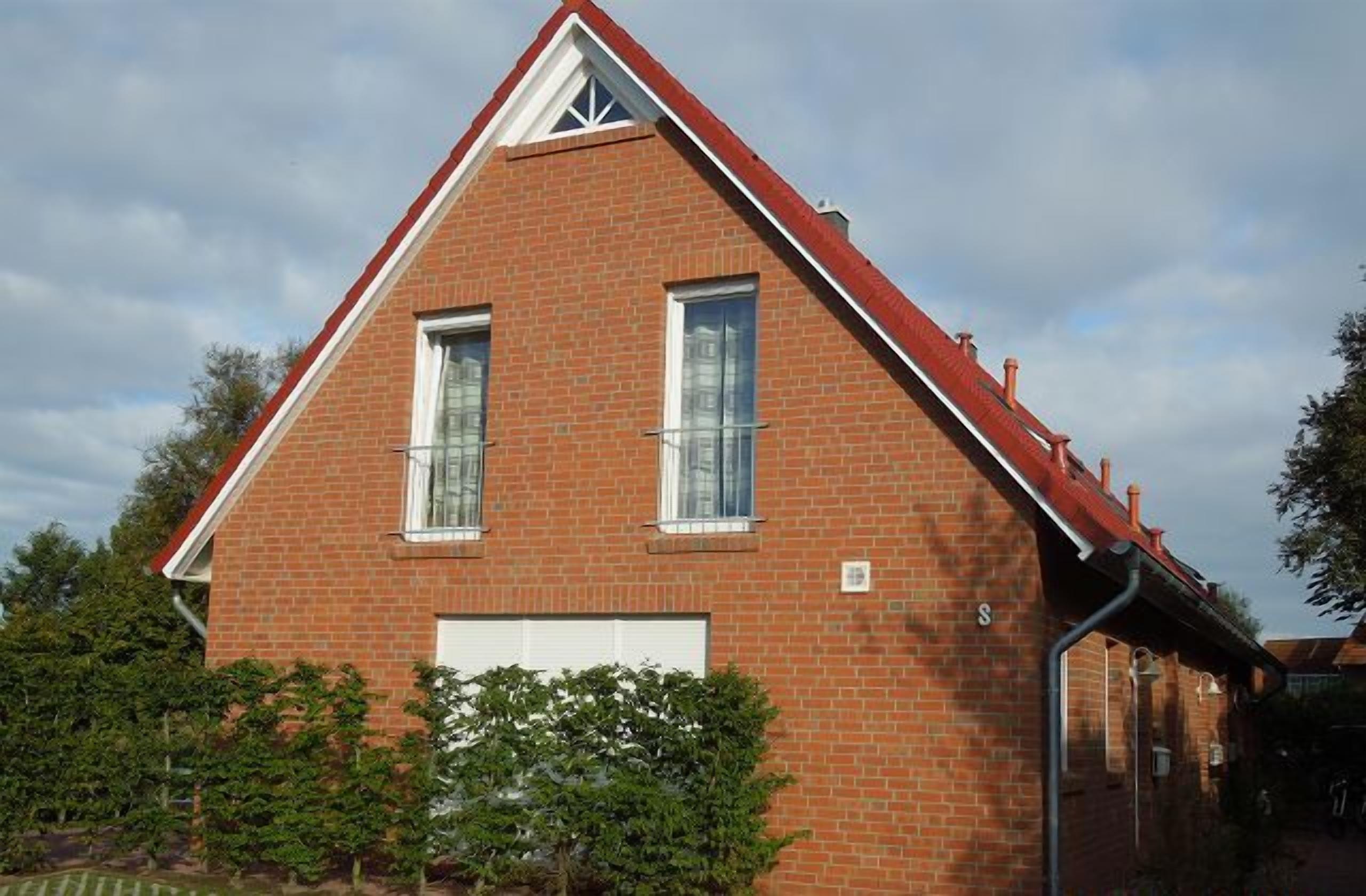 A red brick house with a gabled roof, two windows, and a garage door.