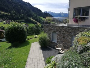 A stone building with a balcony, a paved pathway, and a garden with various plants and a chair. - Relax and enjoy a breathtaking view—your cozy home surrounded by nature (Silbertal)