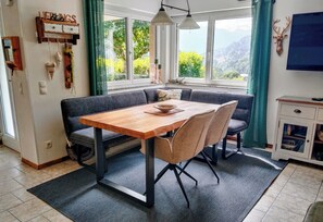 Un comedor con una mesa y sillas de madera, un banco y vistas a zonas verdes a través de amplios ventanales.