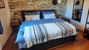 Un dormitorio con suelo de madera, una cama con manta a rayas, dos mesitas de noche y una pared con diseño de ladrillo.
