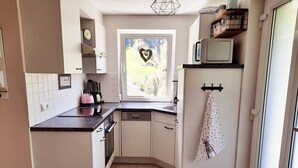 Cocina compacta con armarios blancos, encimera negra, ventana con vista a una casa y microondas en la encimera.