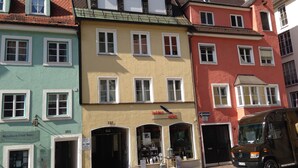 Uma fileira de edifícios coloridos, com estilos arquitetônicos variados, incluindo uma loja com uma placa em língua estrangeira.