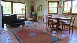 A living room with a sofa, a TV, a dining table with chairs, and a window with curtains. - In the southern Black Forest. Pure nature, close to the lake, family-friendly (Baden-Württemberg)