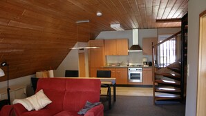 Un interior moderno con un sofá rojo, techo de madera, zona de cocina y una escalera.