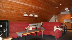 Una habitación acogedora con techo de madera, un sofá rojo, una mesa de comedor y una zona de cocina.