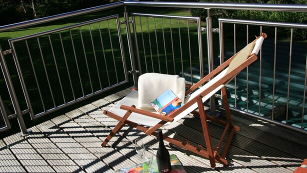 Una terraza con una silla de salón, una botella y un libro.