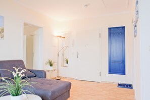 A room with a grey sofa, a small table with a plant, a blue door, and a wooden floor.