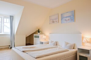 A bedroom with a bed, bedside tables, a nightstand, a lamp, and two wall-mounted paintings.