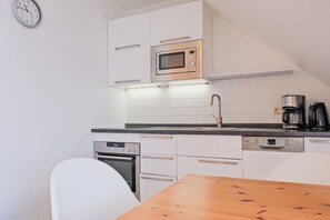 A modern kitchen with white cabinetry, a stainless steel microwave, a built-in oven, a coffee maker, and a wooden table.