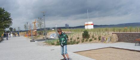 Un chemin pavé où une personne fait du skateboard, un mur de briques et une zone herbeuse avec un banc.